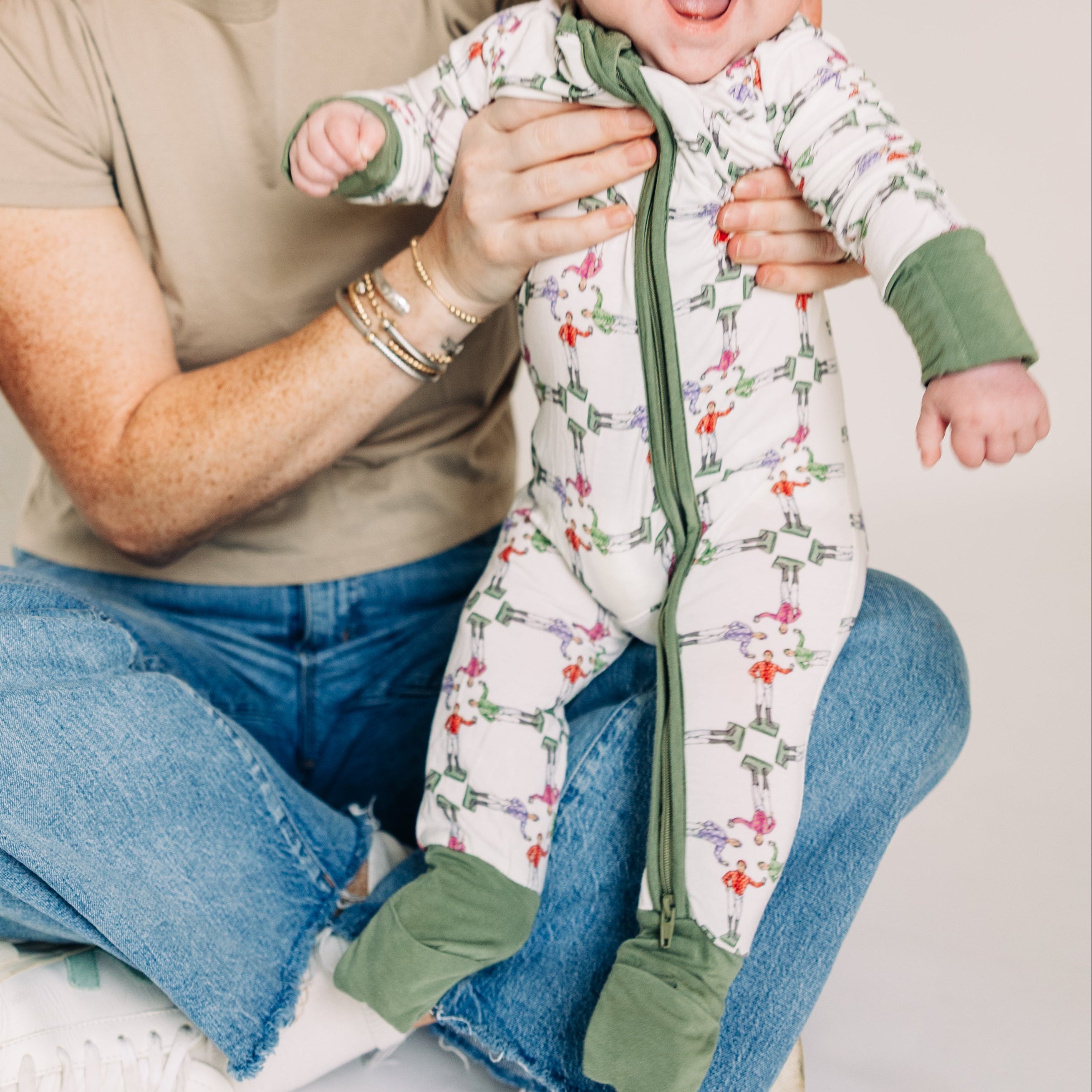 Woman holding a baby wearing a floral onesie against a plain background
