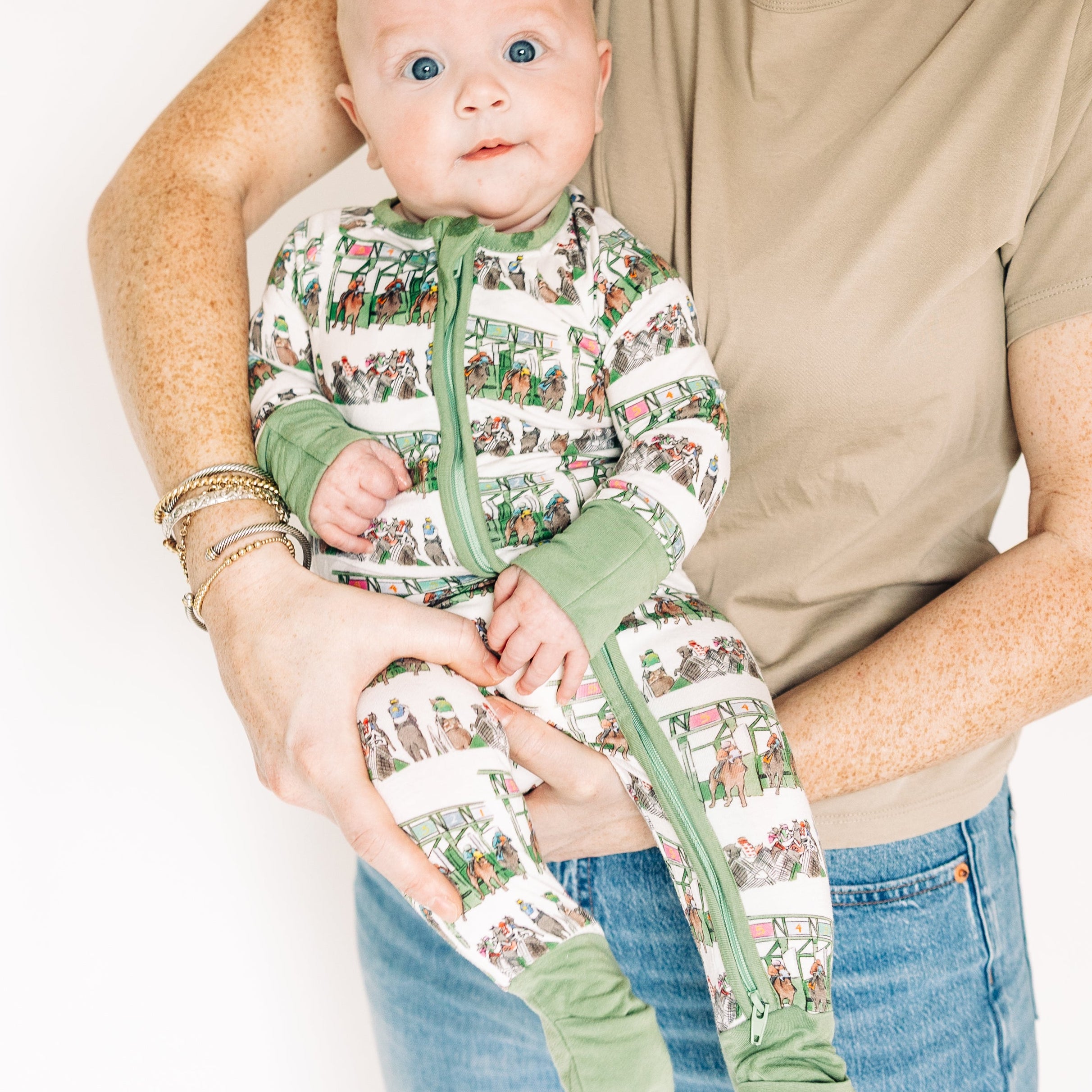 Woman holding a baby wearing a green and white patterned outfit against a plain background