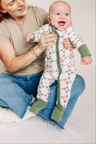 Woman holding a baby wearing a floral onesie against a plain background