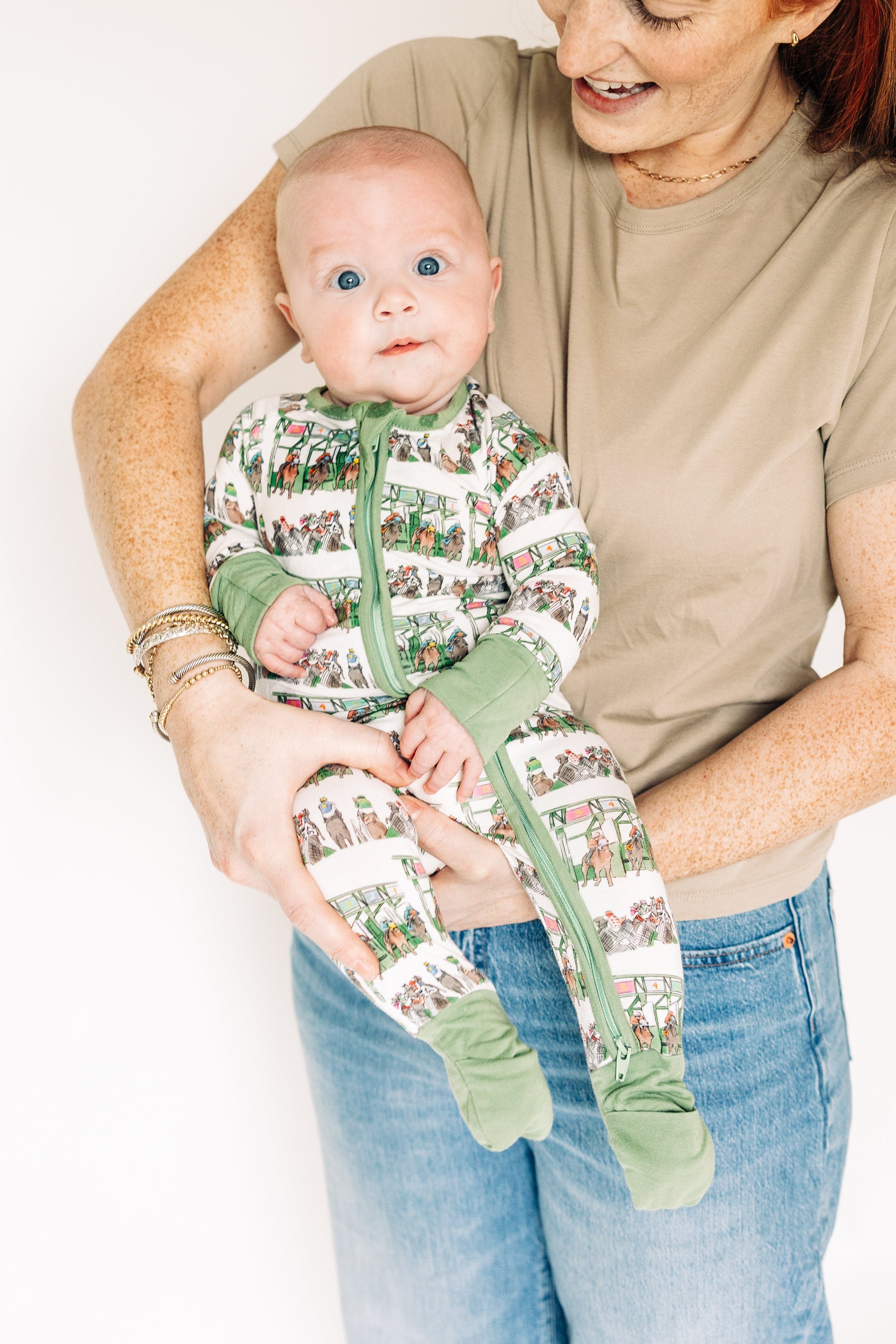 Woman holding a baby wearing a green and white patterned outfit against a plain background